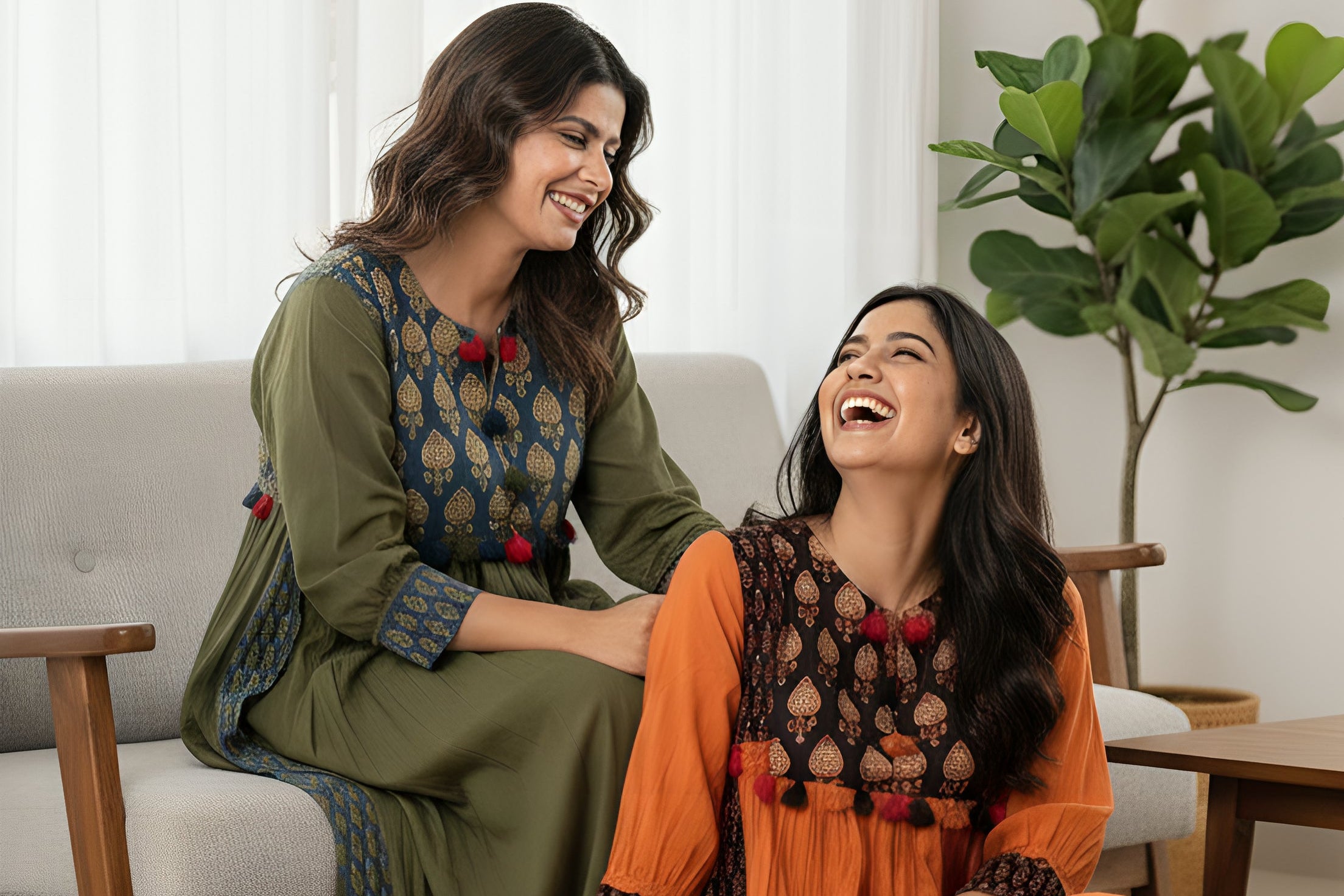 Two women in traditional outfits sitting on a couch in a living room.