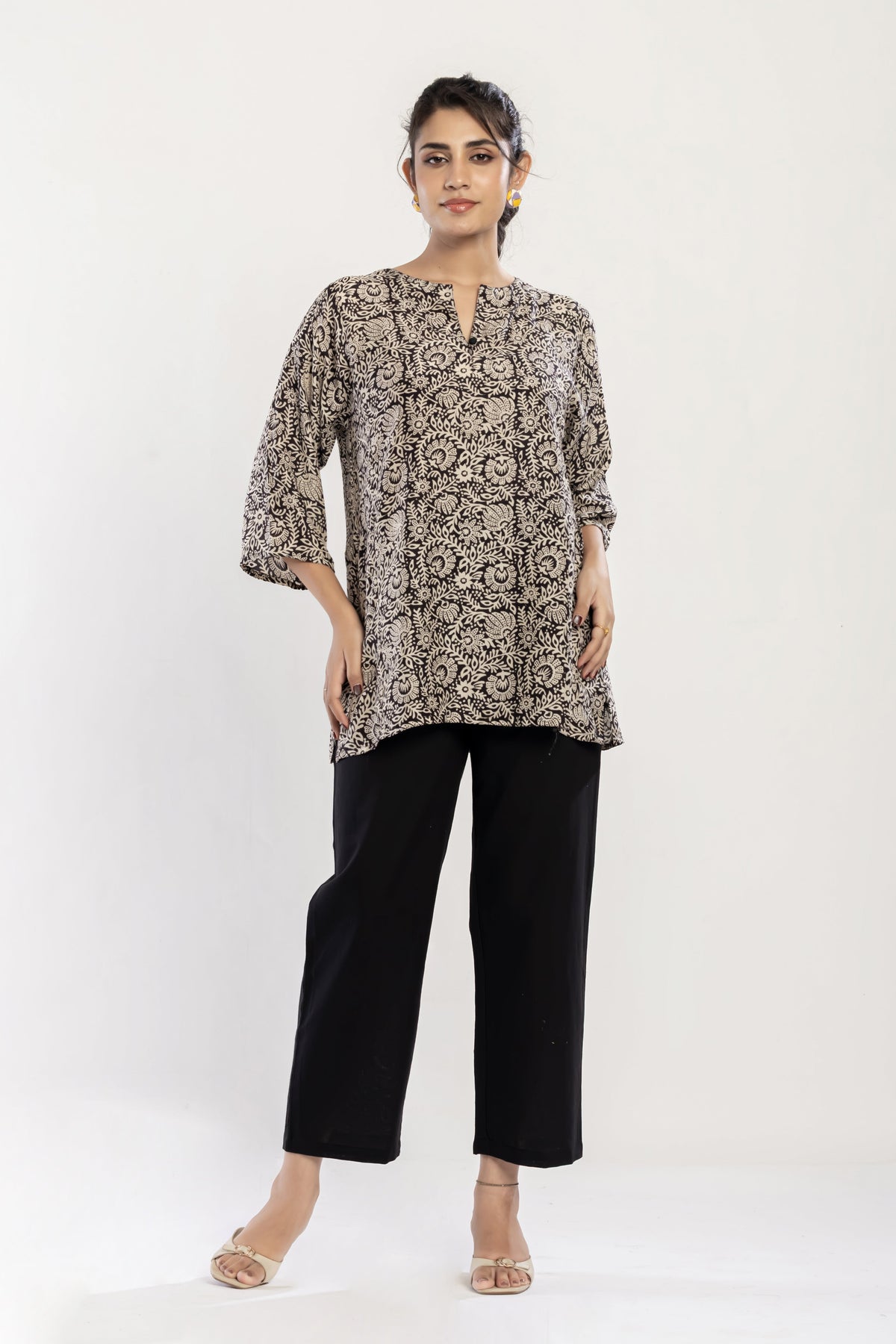 Woman wearing a patterned top and black pants on a white background