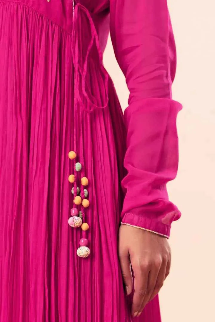 Close-up of a bright pink dress with colorful pom-pom details on a beige background