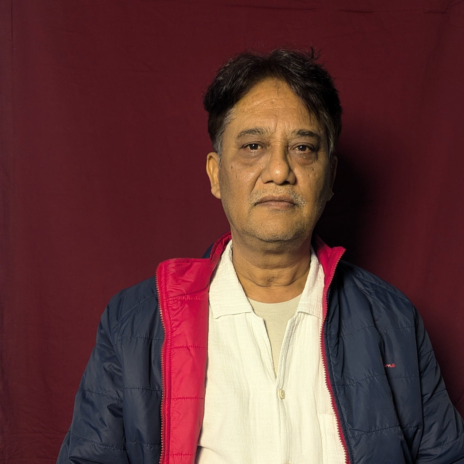 Person wearing a blue jacket with red lining and white shirt against a red background