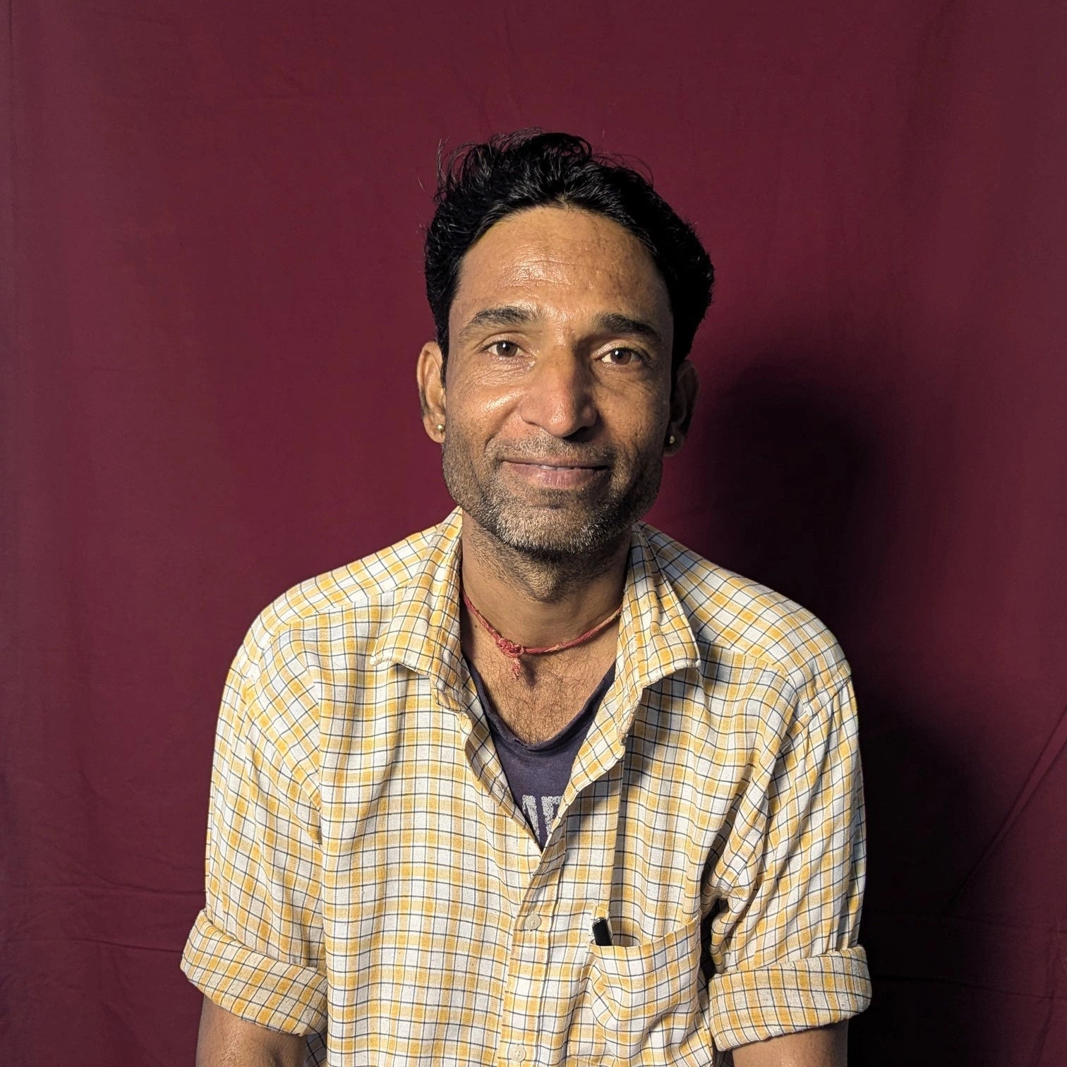 Man wearing a yellow checkered shirt and white pants sitting against a red background
