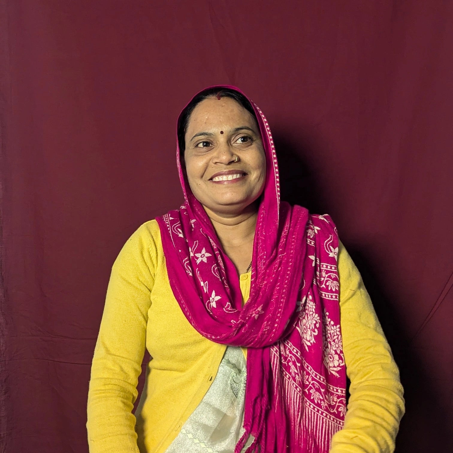 Woman wearing a yellow top and pink scarf against a maroon background