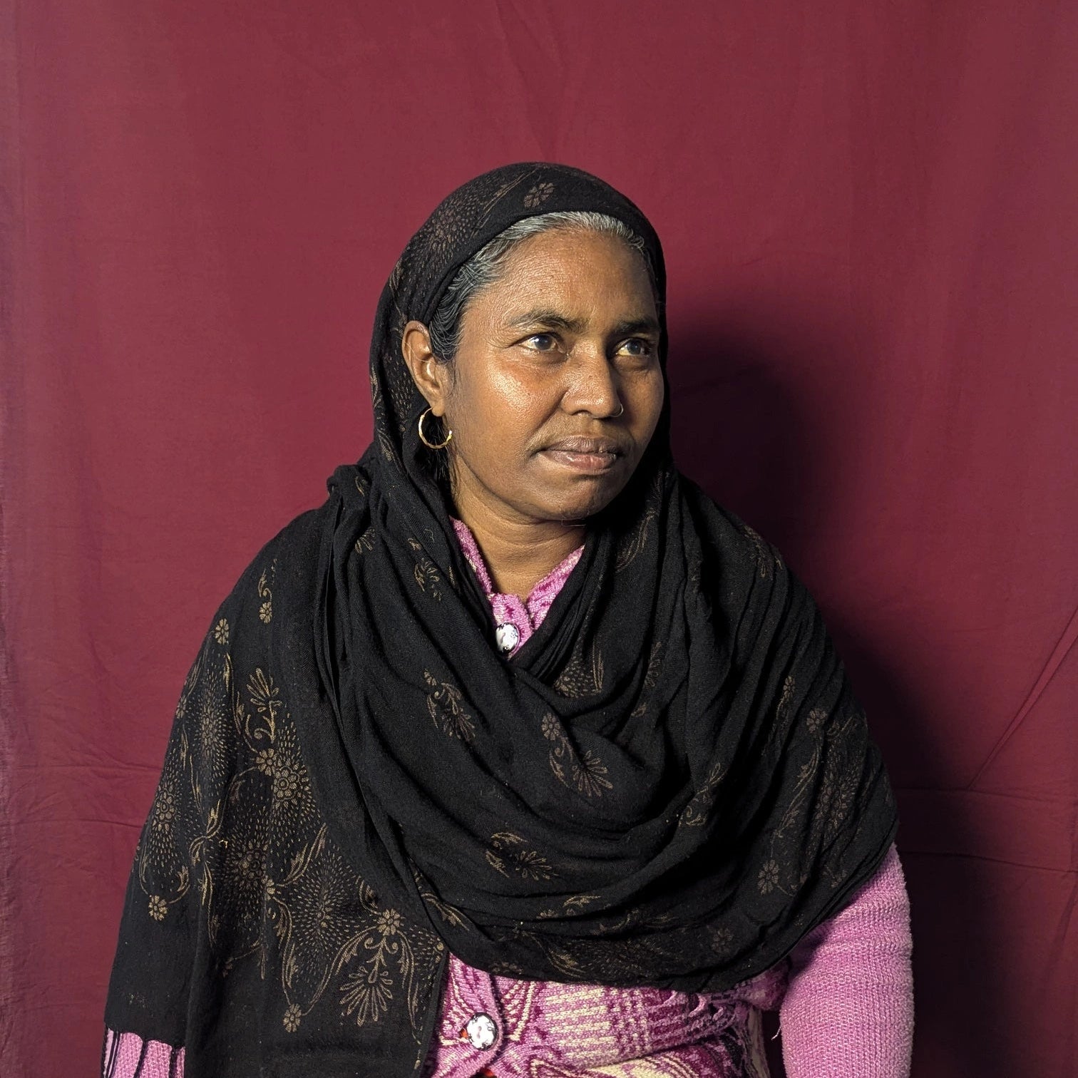 Woman wearing a black headscarf and patterned dress against a red background