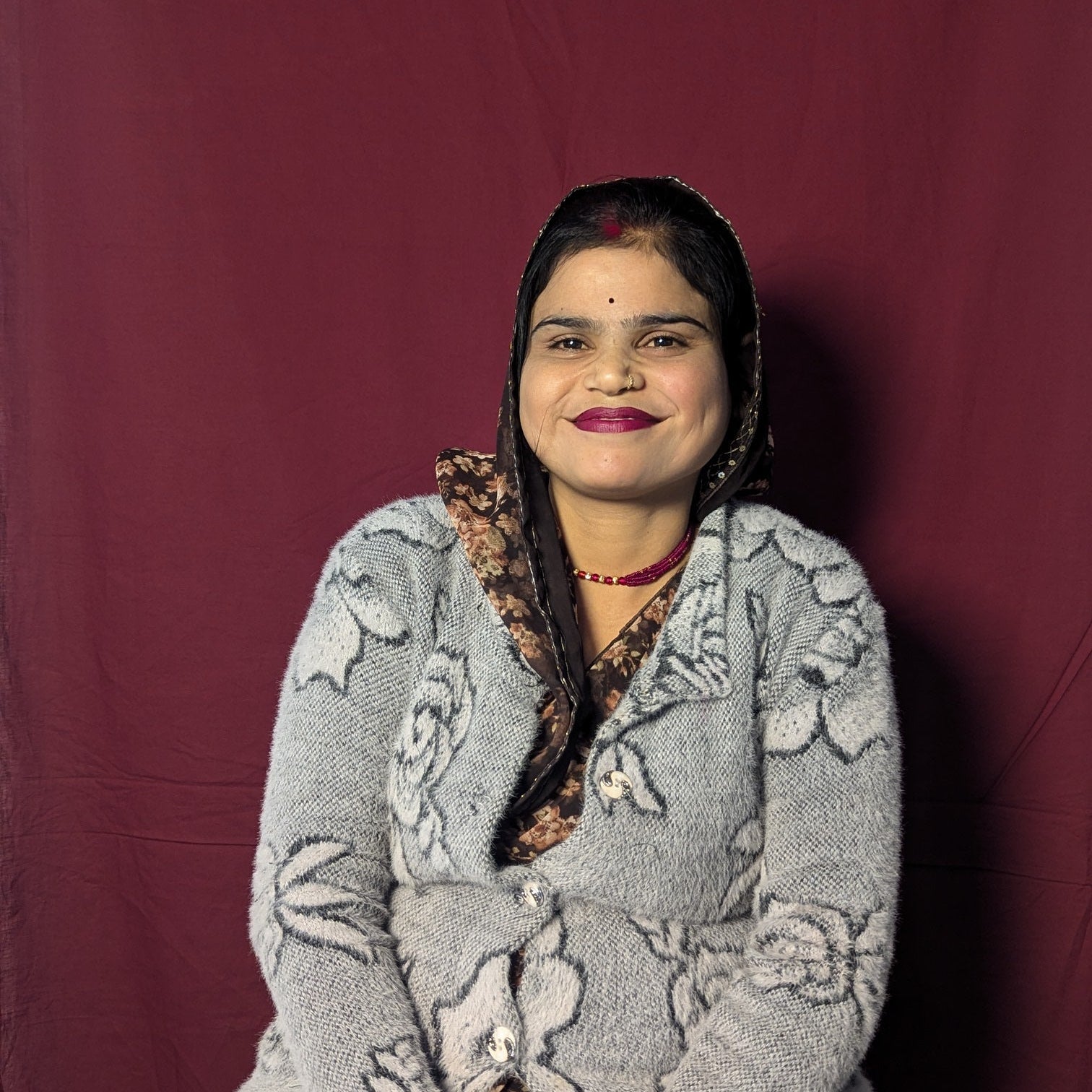Woman wearing a gray floral-patterned sweater over a patterned dress against a maroon background