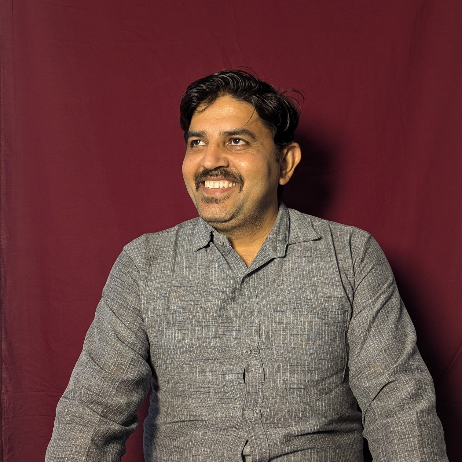 Man wearing a gray shirt and blue jeans against a red background