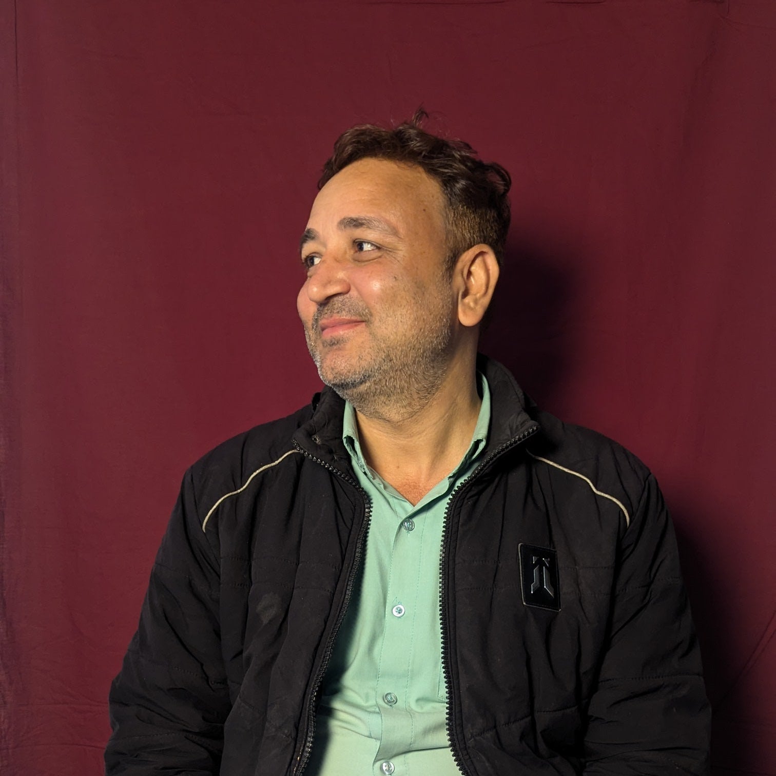 Man wearing a black jacket and light green shirt against a red background