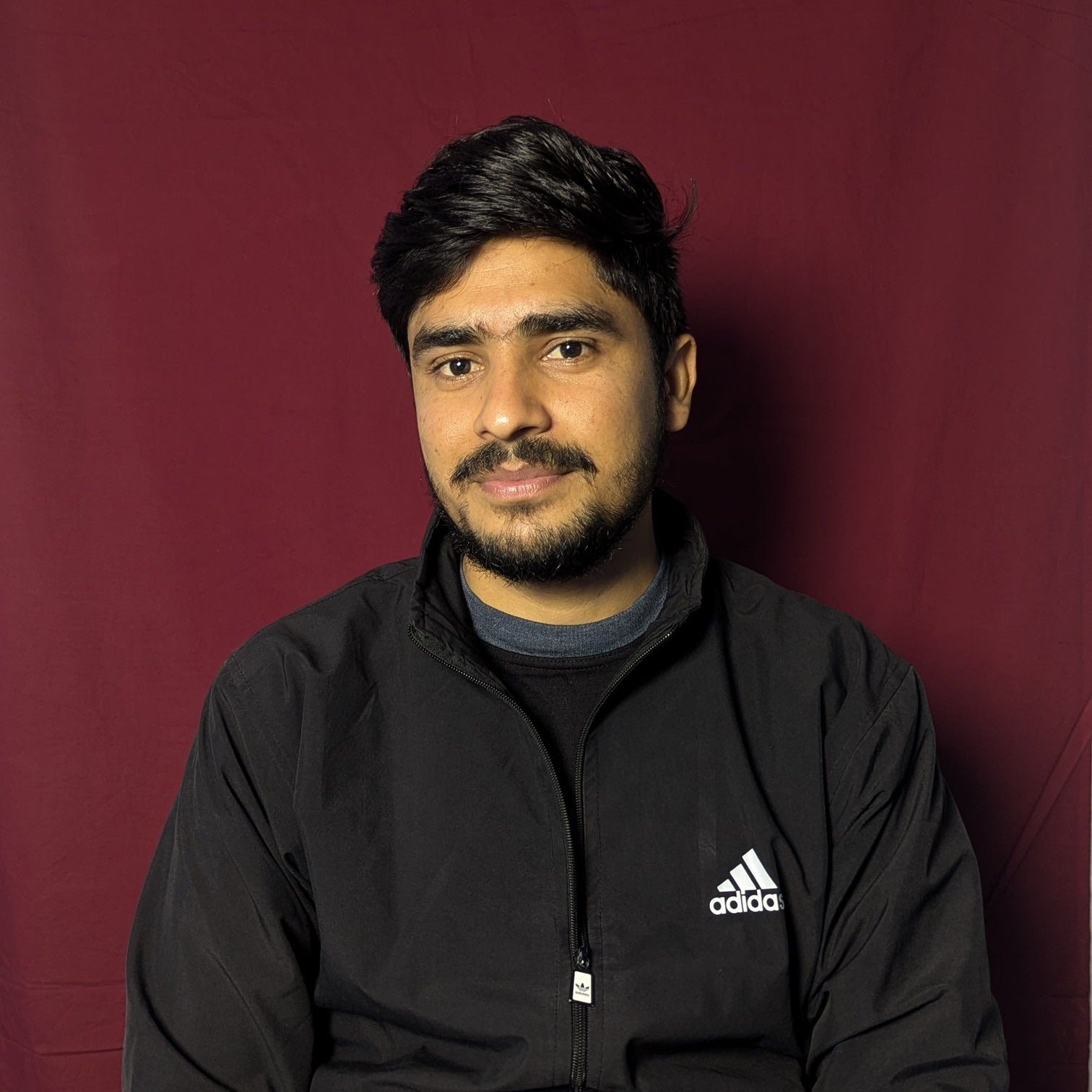 Person wearing a black Adidas jacket against a red background