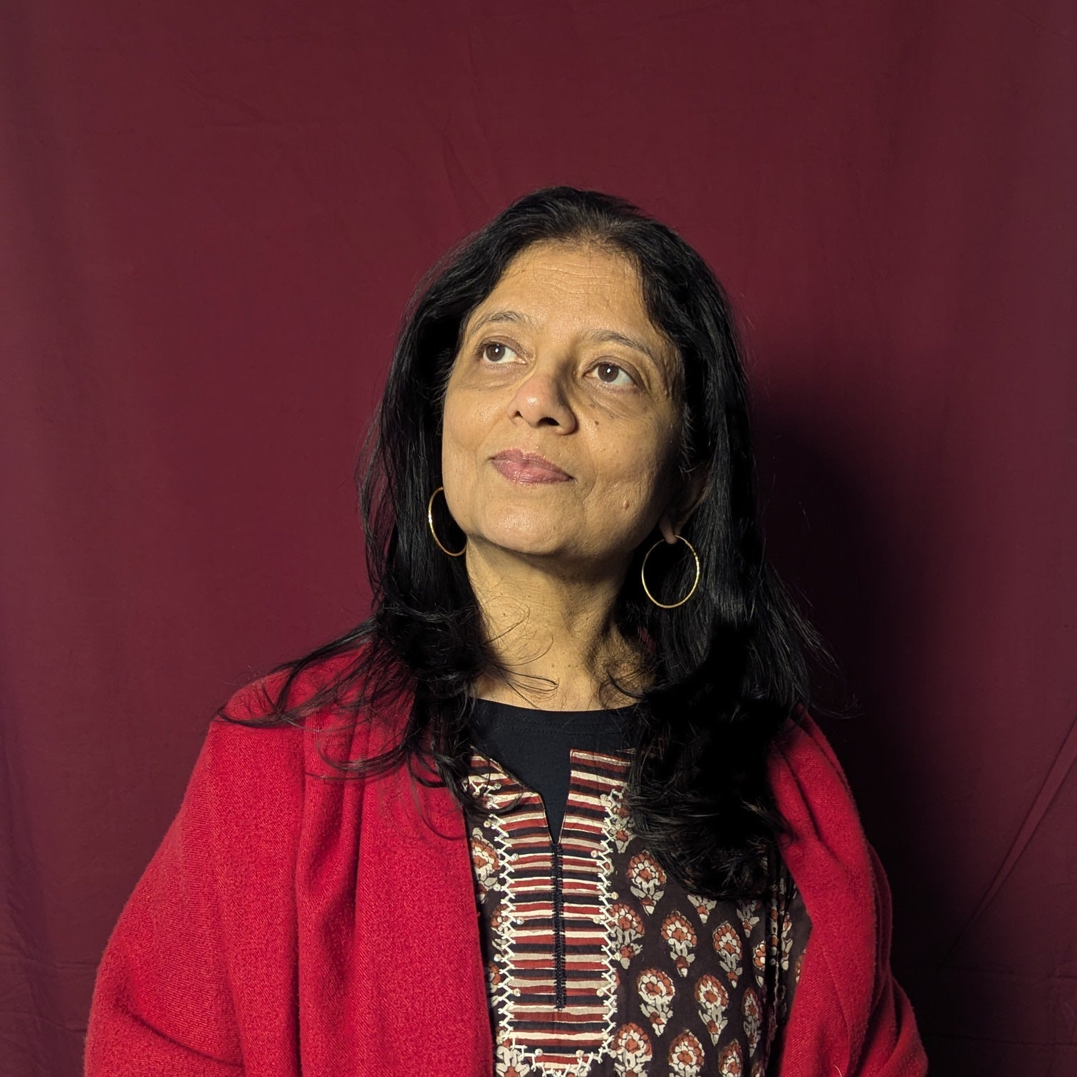 Woman wearing a red shawl over a patterned dress against a maroon background