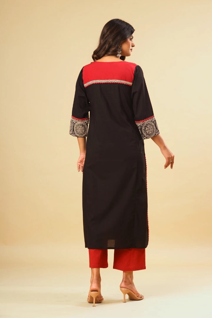 Woman wearing a black and red traditional outfit with intricate patterns on a beige background