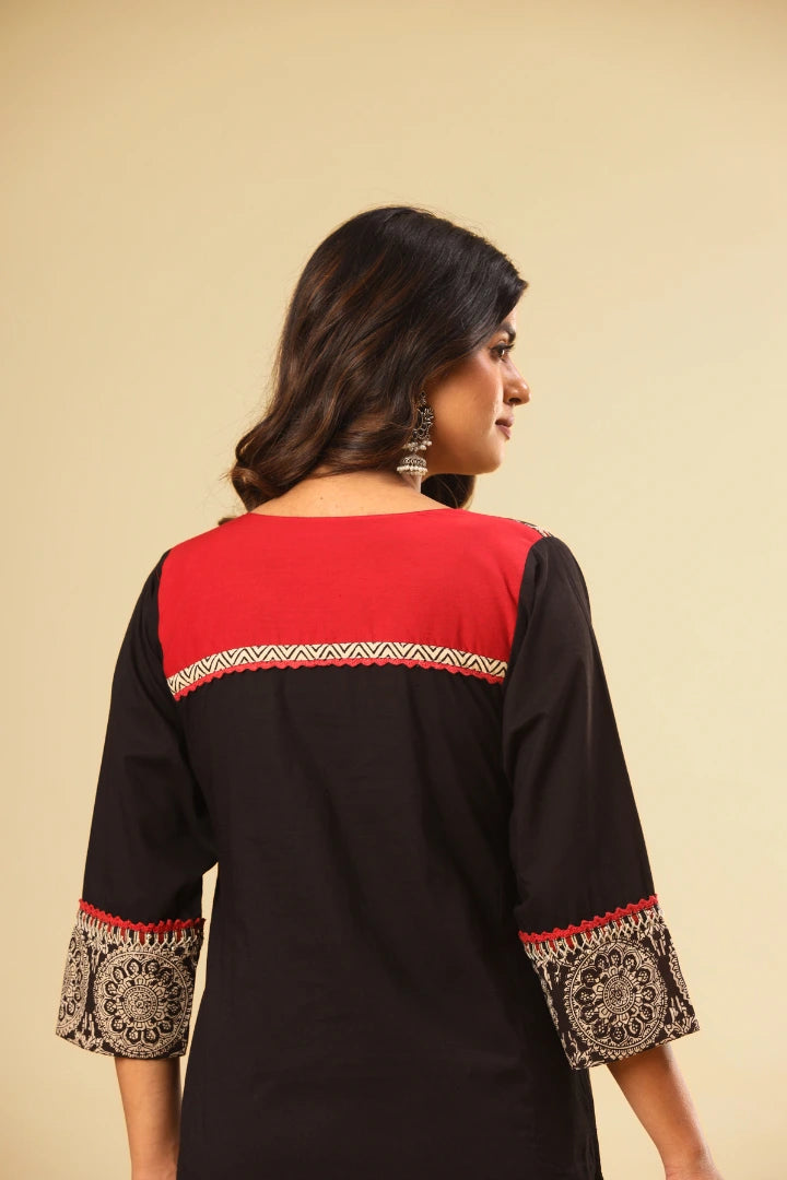 Woman wearing a black and red top with intricate designs on a beige background
