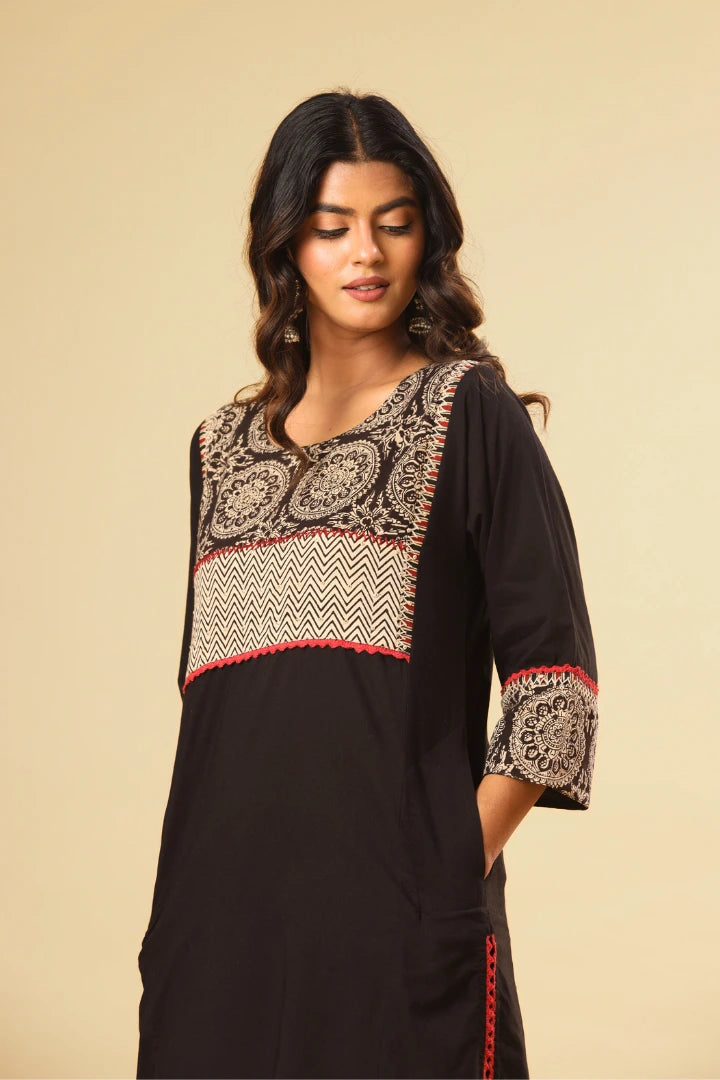 Woman wearing a black dress with patterned accents on a beige background