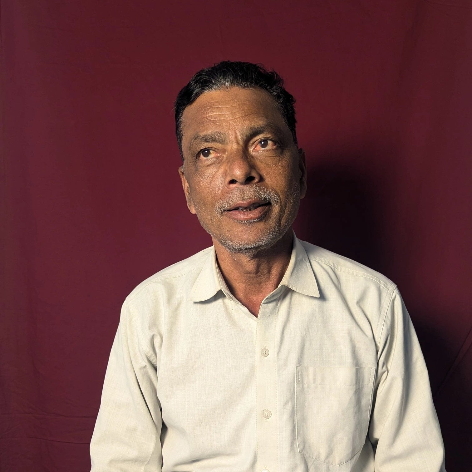 Man wearing a light-colored shirt against a red background